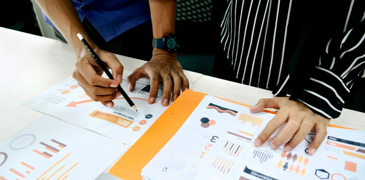 Zwei Personen werten gemeinsam Business-Intelligence-Daten aus und besprechen Diagramme und Kennzahlen auf einem Schreibtisch.